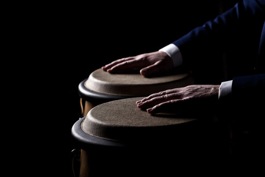 Hands of a musician playing on bongs in dark tones