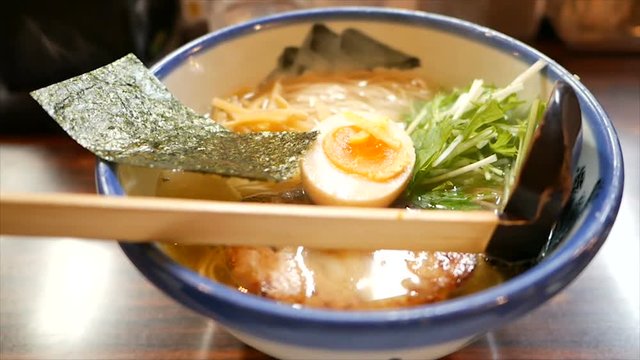 bowl of hot ramen or noodles soup in japan, with grilled pork, seaweed, egg and green vegetable on wooden table