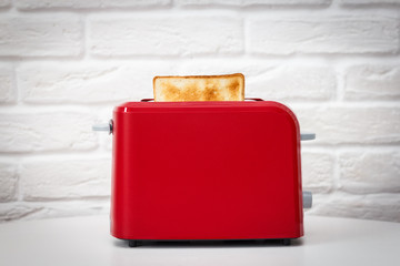 Red toaster with toasted bread for breakfast inside. White table. White brick wall. - 183708230