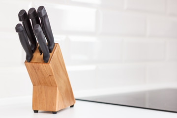 Knifes in wooden block on white kitchen table. White tile background.