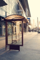 Bus stop near a shopping mall, sign and trees against the sky with clouds on a background. City transport system.