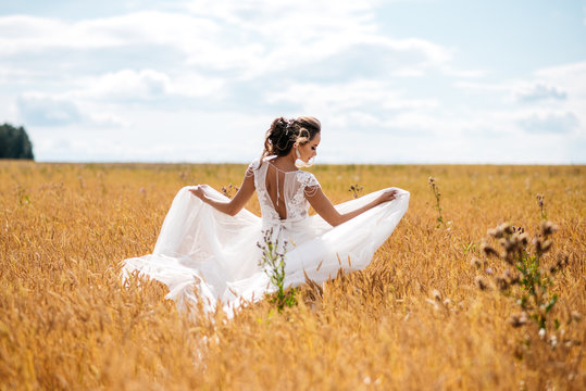 A beautiful bride in wedding dress is dancing alone in a field of wheat. View from the back
