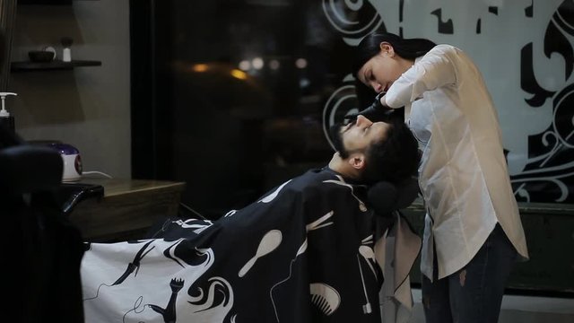 Female barber cuts the beard hair of the male client