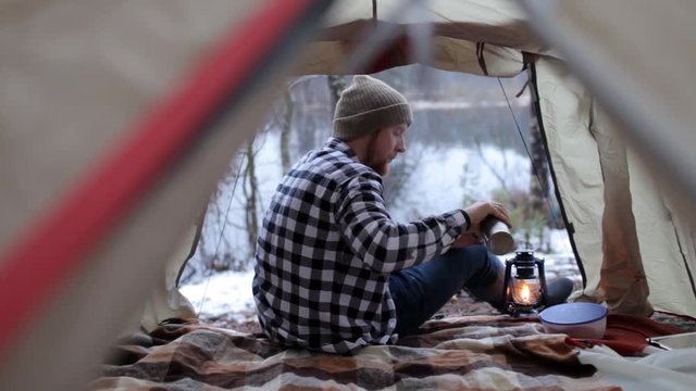 bearded man drinking tea in a tent in a winter forest