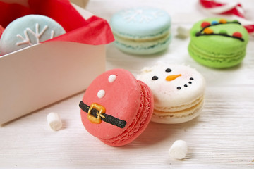 Traditional christmas themed french macaroons sweets in the form of snowman, snowflake, christmas tree and santa's belly with candy cane and white marshmallows on the white wooden table.  Close up.