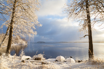 Beautiful view of Lake Pyhäjärvi, snowy ground, rowboats and trees and snow falling from trees on...