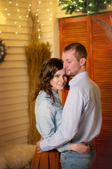 Loving couple in blue shirts hugging in the new year interiors with glowing garlands