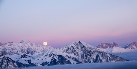 full moon rising in the evening sky in the Swiss Alps over a winter mountain landscape near Klosters