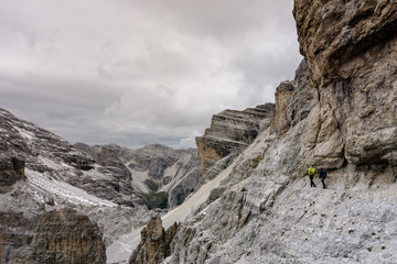 two climbers walking along a narrow and exposed rock ledge on a Via Ferrata in the Italian Dolomites on an overcast day in autumn