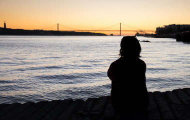 Young girl watching amazing sunset on Ponte 25 de Abril Bridge, (25th of April Bridge) at Lisbon. Portugal