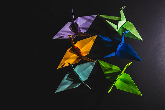 Cranes origami composed of paper of different colors. Cranes are made in origami technique on a dark background. Cranes of origami, lined up on the right side.