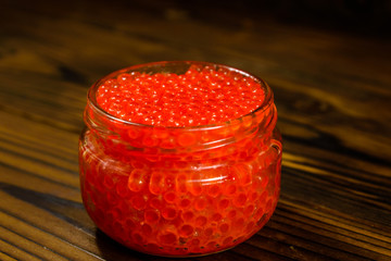 Red caviar in glass jar on wooden table