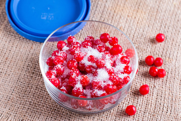 Red juicy berries of a viburnum with sugar in a glass jar on a wooden background. For making jam, tea