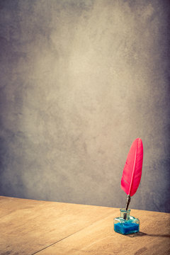 Vintage old red quill pen with inkwell on wooden table front concrete wall background. Retro style filtered photo