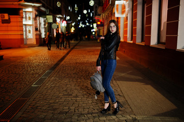 Night portrait of girl model wear on glasses, jeans and leather jacket, with backpack , against lights of city streets.