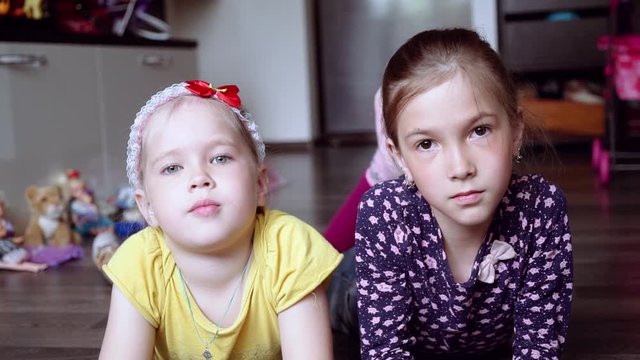 little girls lie on the floor and look at the camera. two sisters.