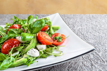 salad with avocado, mozzarella, Basil and cilantro in a beautiful plate stands on the table