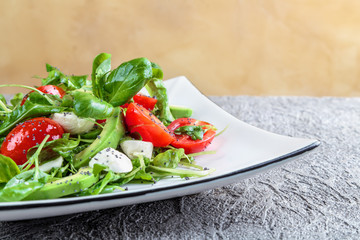 salad with avocado, mozzarella, Basil and cilantro in a beautiful plate stands on the table