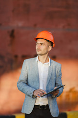 Handsome unshaven successful business man in gray suit, protective construction orange helmet...