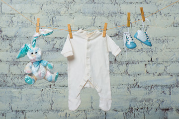 Children's white bodik, boots, panties and a toy rabbit dry on a rope against a white brick wall.