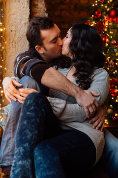 Couple of lovers hugs sitting on the windowsill in the Christmas loft studio. guy is hugging the girl.