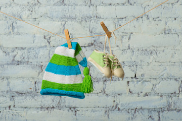 Baby cap and sneakers will dry on a rope on a white brick wall.