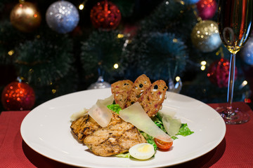 Fototapeta na wymiar Caesar salad with chicken and parmesan cheese. Christmas or New Year's Eve dinner. Dinner with a Christmas tree. A festive dish for Christmas and New Year with champagne. Christmas tree background