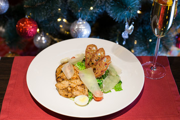 Caesar salad with chicken and parmesan cheese. Christmas or New Year's Eve dinner. Dinner with a Christmas tree. A festive dish for Christmas and New Year with champagne. Christmas tree background