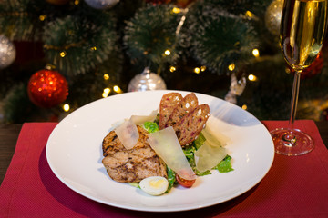 Caesar salad with chicken and parmesan cheese. Christmas or New Year's Eve dinner. Dinner with a Christmas tree. A festive dish for Christmas and New Year with champagne. Christmas tree background