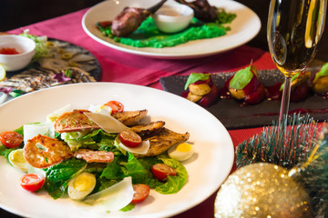 Caesar salad with chicken and parmesan cheese. Christmas or New Year's Eve dinner. Dinner with a Christmas tree. A festive dish for Christmas and New Year with champagne. Christmas tree background