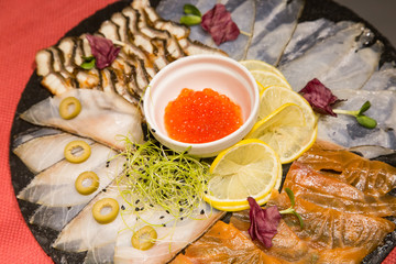 Plate with fish snacks. Fish cut for a festive dinner. Salmon, tuna, red caviar, white fish, eel, lemon. Christmas or New Year's Eve dinner. Dinner with a Christmas tree. A festive dish for Christmas 