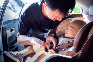 asian father helps his cute little asian 1 year old toddler baby boy child to fasten belt on car...