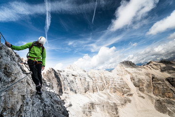 male mountain climber in a green jacket on an exposed Via Ferrata in the Dolomites in Italy with a...