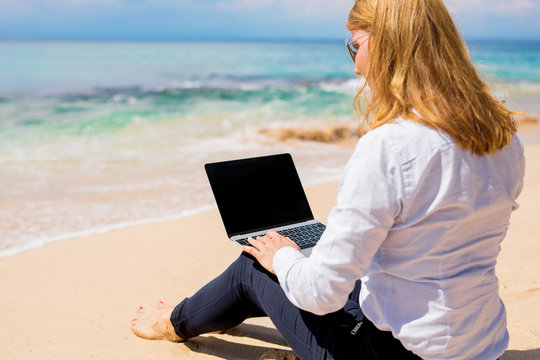 Businesswoman sitting on the beach and working with laptop computer