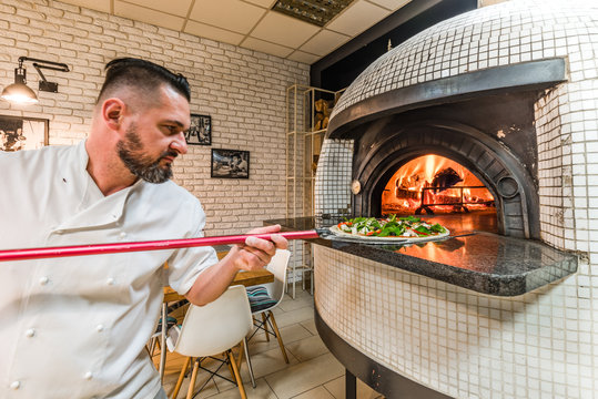 Bearded man baking pizza in woodfired oven