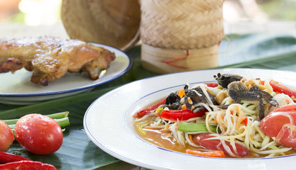 Papaya salad mix with salted crab (Som tum) with grill chicken and sticky rice in bamboo basketry and vegetables on banana leaf Thai food
