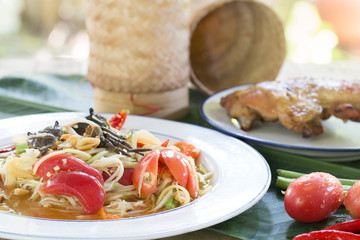 Papaya salad mix with salted crab (Som Tum) with grill chicken and sticky rice in bamboo basketry and vegetables on banana leaf Thai food