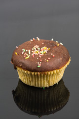Vanilla cupcakes with chocolate cream and colorful sprinkles above black reflections background