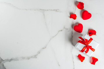 Valentine's day background with rose flower petals, white wrapped gift box with red ribbon and holiday red candle, on white marble background, copy space top view