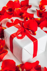 Valentine's day concept, with rose flower petals and white wrapped gift box with red ribbon, on white marble background, copy space