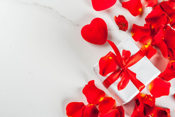 Valentine's day concept, with rose flower petals and white wrapped gift box with red ribbon, on white marble background, copy space top view