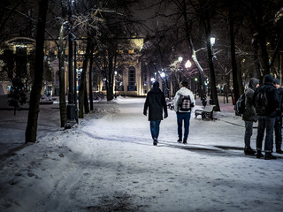 night snowy winter  landscape in the alley of city park with walking people