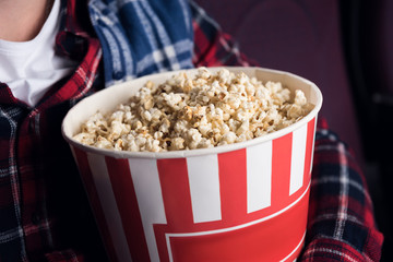 cropped view of man holding big basket of popcorn in movie theater