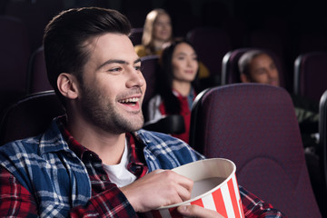 smiling handsome man with popcorn watching movie in cinema