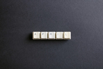 April month word is written with computer keys button. Flat lay view from above on the table with computer keyboard keys buttons on a dark background.