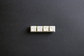 June month word is written with computer keys button. Flat lay view from above on the table with computer keyboard keys buttons on a dark background.