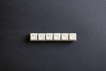 August month word is written with computer keys button. Flat lay view from above on the table with computer keyboard keys buttons on a dark background.