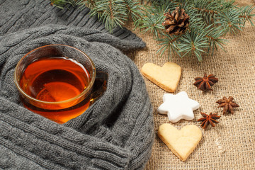 Cup of tea with slice of lemon wrapped up in wool scarf, gingerbread cookies in star and heart...