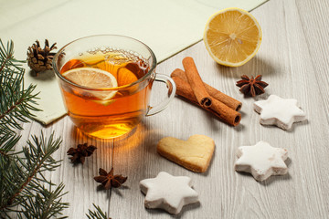 Cup of tea with slice of lemon, gingerbread cookies in star and heart shape, natural fir tree branches with cone and spices