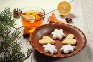 Cup of tea with slice of lemon, gingerbread cookies in star and heart shape on plate, natural fir tree branches with cone and spices